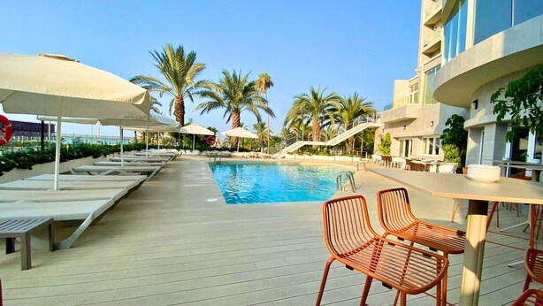Un espace aménagé au bord de la piscine, avec des chaises longues, des parasols et une piscine.