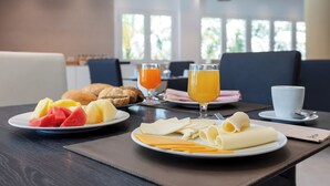 Une table dressée pour le petit-déjeuner, avec des assiettes de fruits, de fromage et des croissants, ainsi que des verres de jus d’orange et une tasse de café.