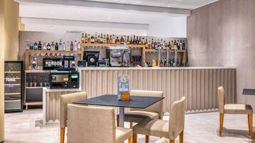 Zona de bar con mostrador, varias botellas, máquina de café y asientos.