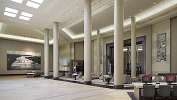 A spacious lobby with high ceilings, large columns, and a modern design. There are several seating areas and a large artwork on the wall.