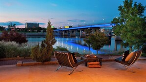 An outdoor seating area with two chairs and a table, overlooking a river with a bridge in the background. - Little Rock Marriott (Little Rock)