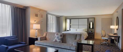 A hotel room with a bed, two sofas, a coffee table, a desk, and a chair.