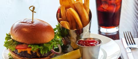 Un hamburger avec des frites et un cornichon sur une assiette, un verre de thé glacé et une fourchette posée sur une serviette.