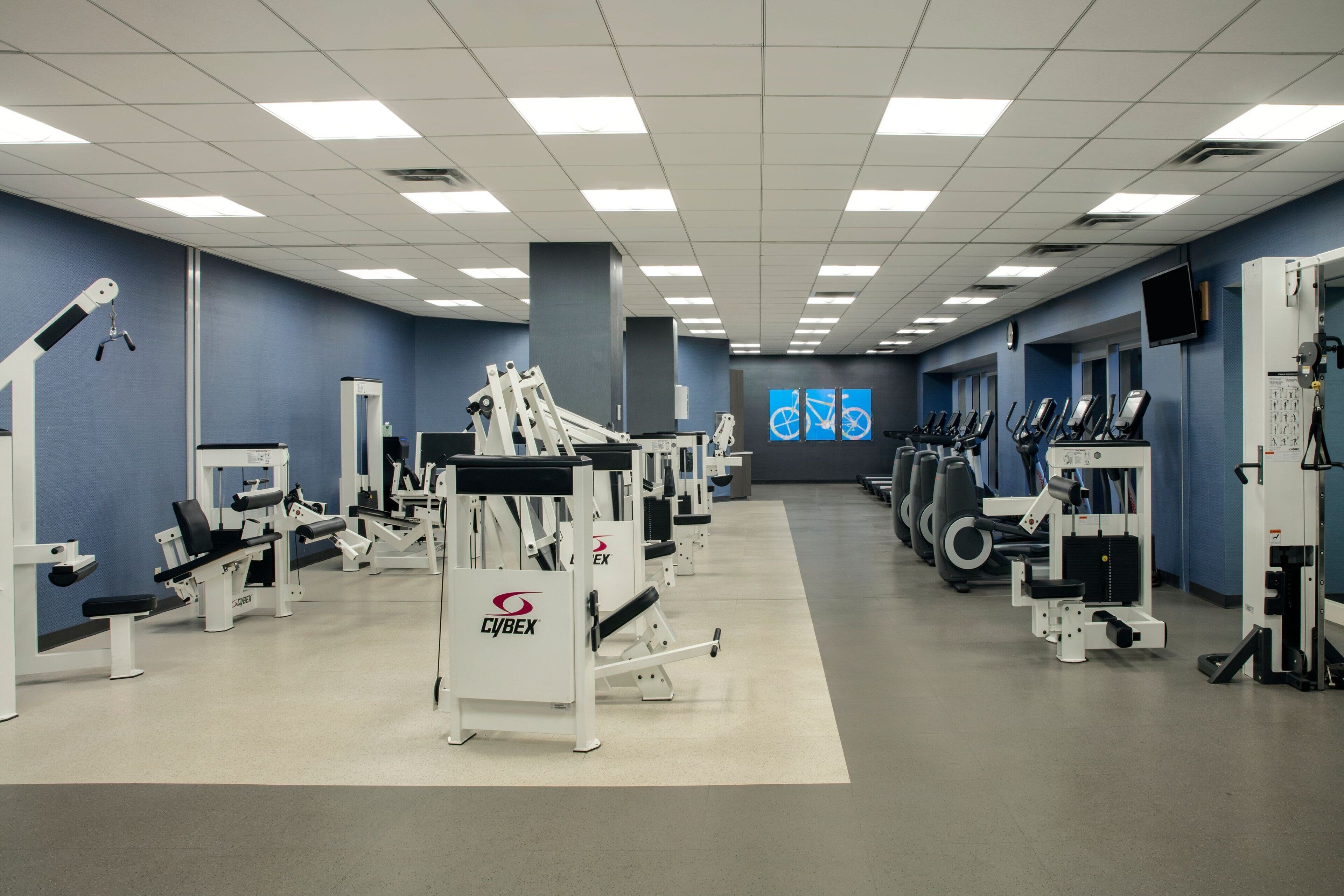 A gym with various exercise machines, a large mirror, and a wall-mounted television.
