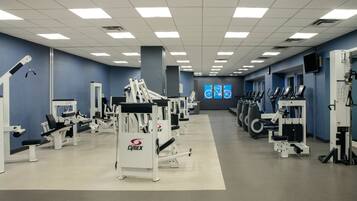 A gym with various exercise machines, a large mirror, and a wall-mounted television.