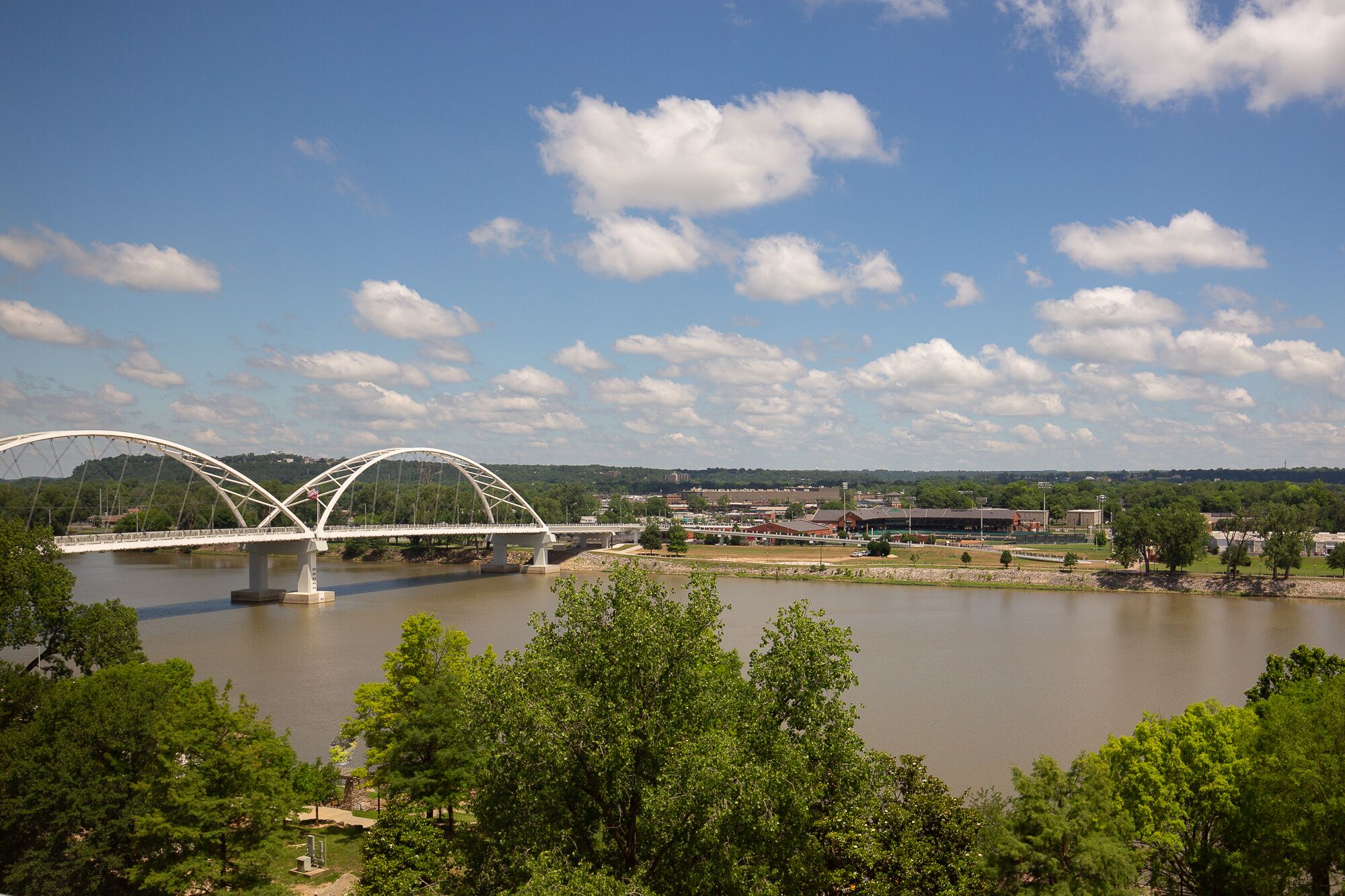 A white arched bridge over a river with a backdrop of trees and buildings.