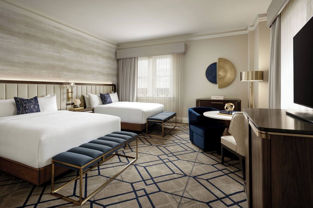 A hotel room with two beds, a desk, a chair, and a TV.