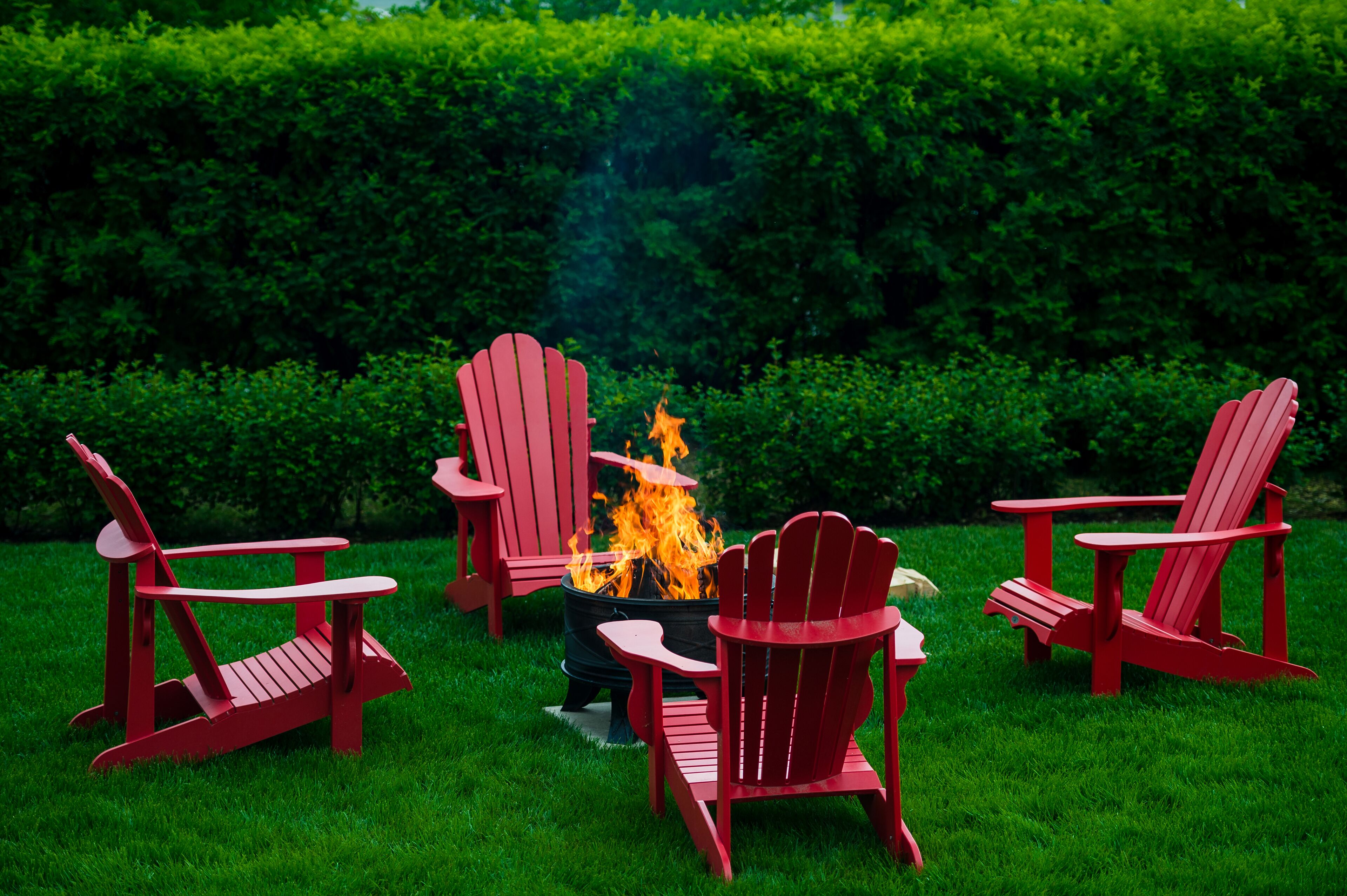 A fire pit with red Adirondack chairs arranged around it in a grassy outdoor area.
