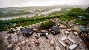 Un espace extérieur aménagé en terrasse, avec des tables et des chaises, offrant une vue sur une rivière et un pont en arrière-plan.