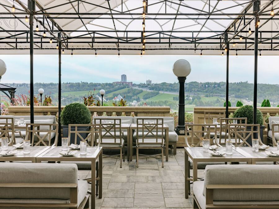 Un espacio de comedor al aire libre con mesas y sillas, una estructura de pérgola y vistas a un horizonte urbano distante.