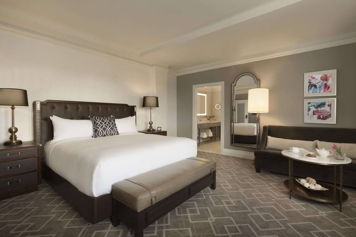 A hotel room with a large bed, bedside tables, a sofa, a small table with a tray, and a mirror.