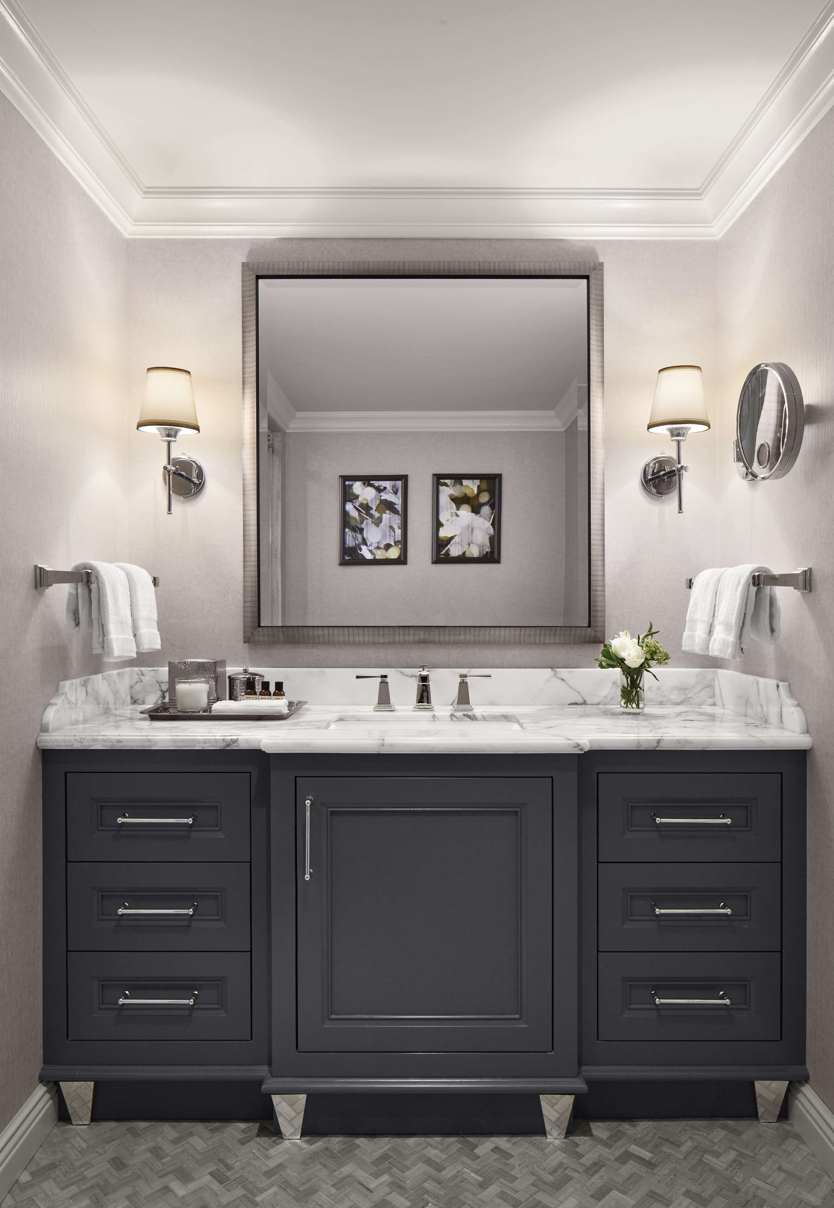 Une salle de bain moderne dotée d’un meuble-lavabo double, d’un plan de toilette en marbre, de meubles de rangement aux couleurs sombres, d’appliques murales et d’un grand miroir.