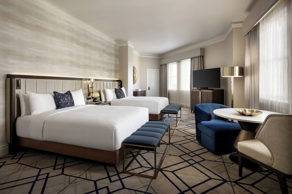A hotel room with two beds, a TV, a desk, and a chair.
