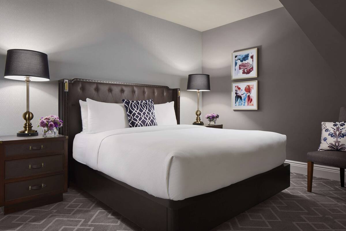 A neatly made bed with a dark headboard, two bedside tables with lamps, and a chair.