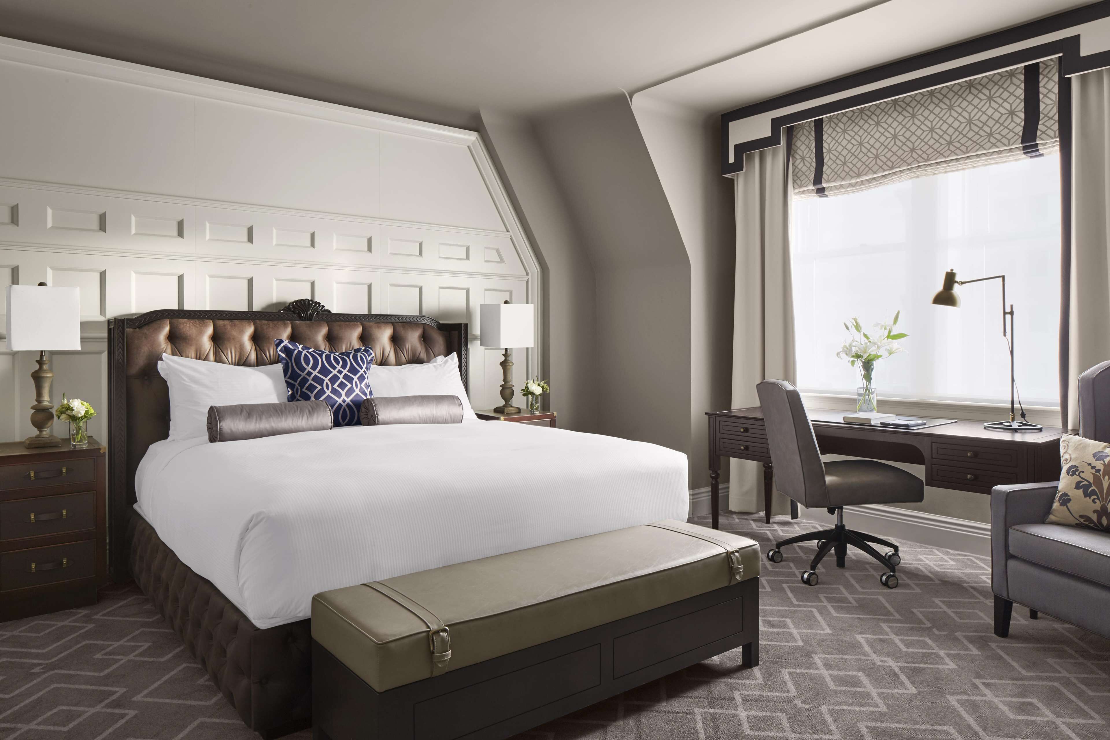 Una habitación de hotel moderna con una cama grande, un escritorio y un ventanal con cortinas.