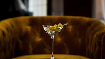 A martini glass with olives on a reflective surface, set against a plush, upholstered chair.