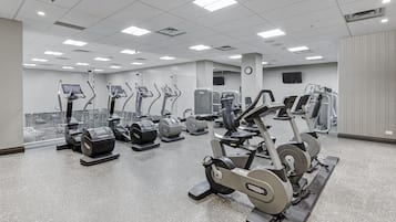 A gym with various cardio and strength training equipment, a large mirror, and a clock on the wall.