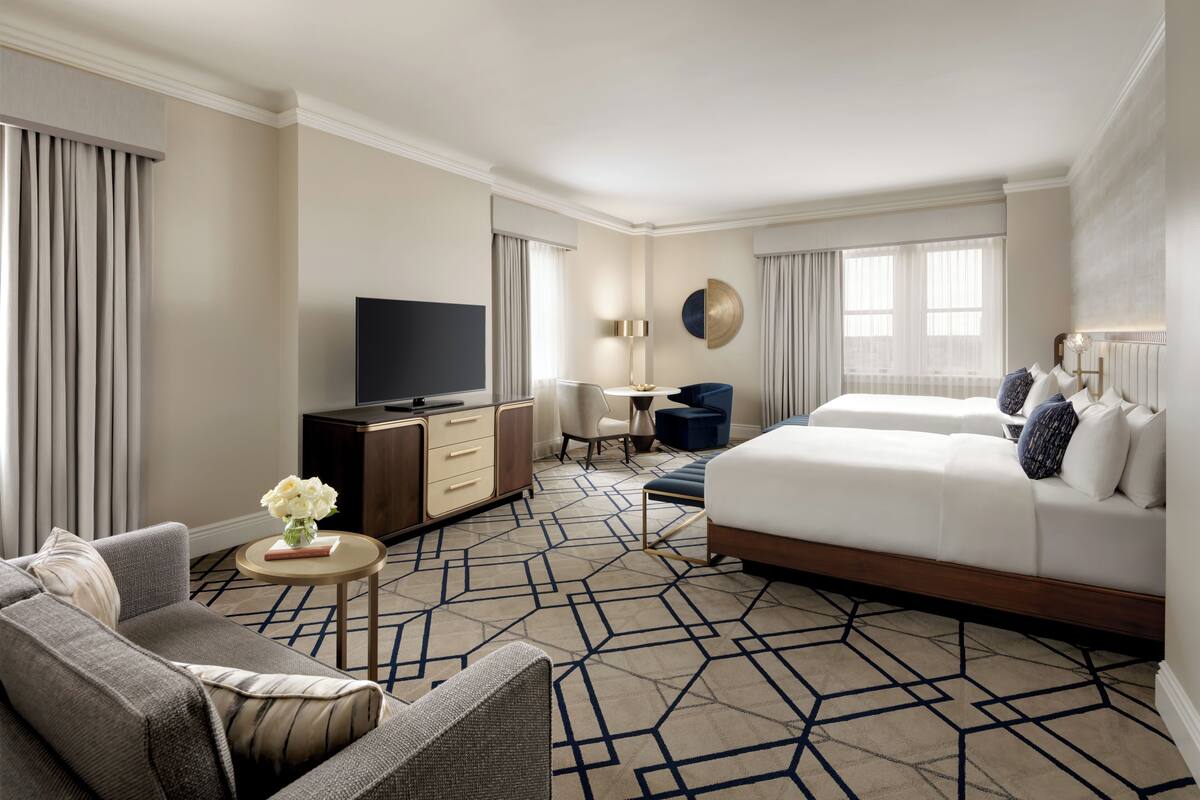 A hotel room with a large bed, a sofa, a desk with a TV, and a small table with a vase of flowers.