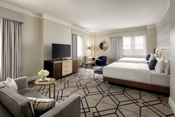 A hotel room with a large bed, a sofa, a desk with a TV, and a small table with a vase of flowers.
