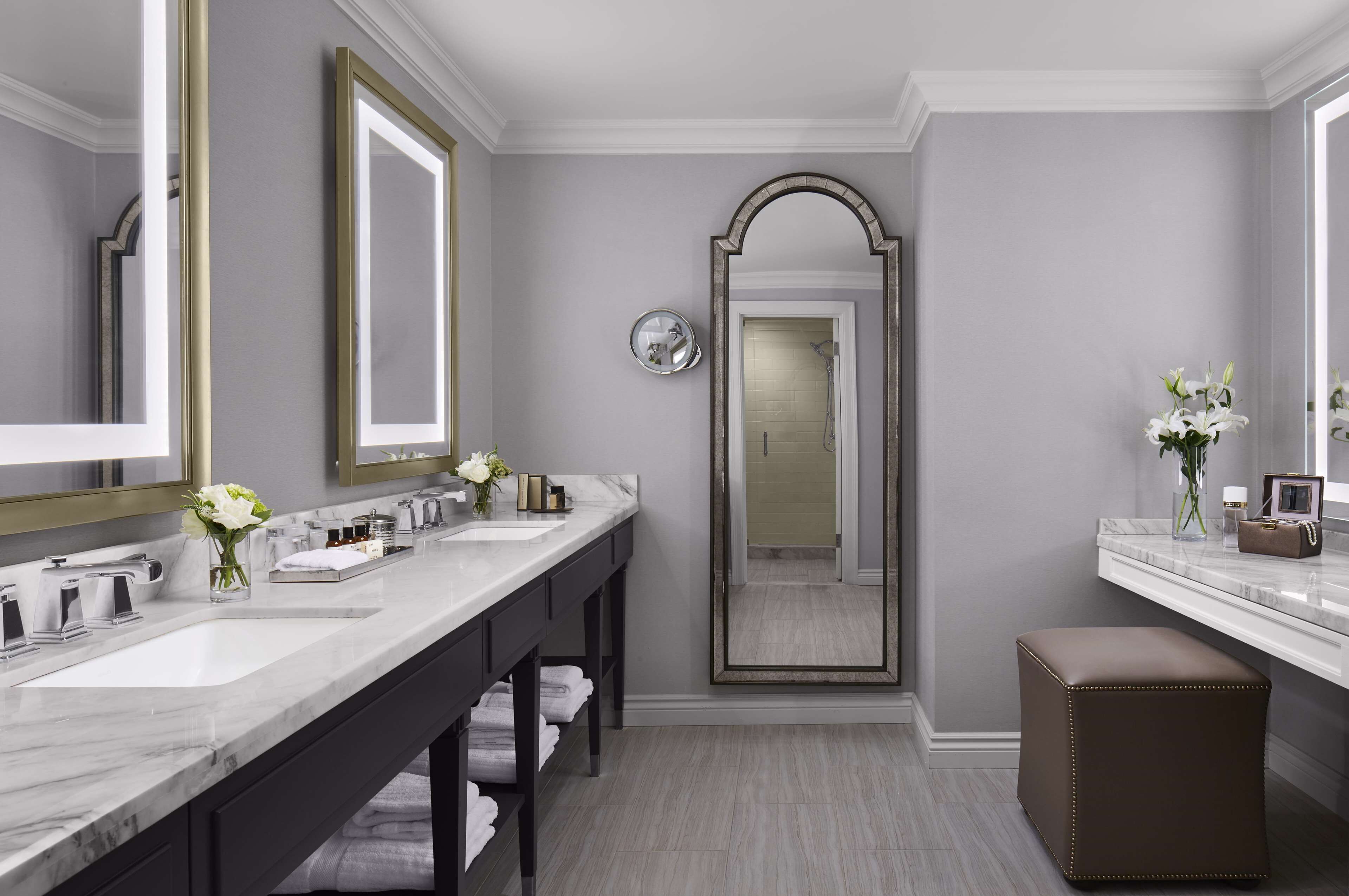 A modern bathroom with two sinks, a large mirror, and a bench.