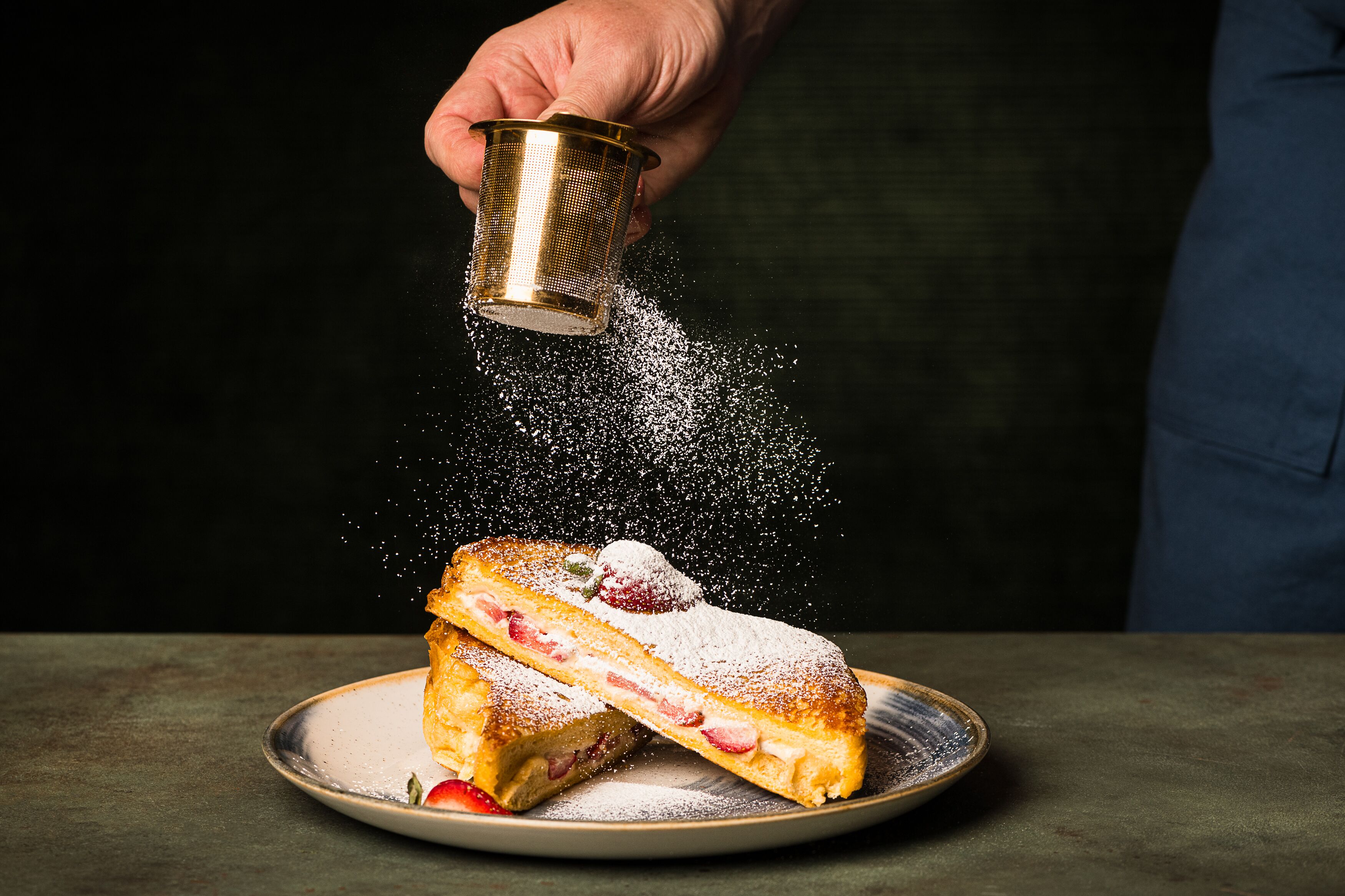 A hand sprinkling powdered sugar on a dessert.