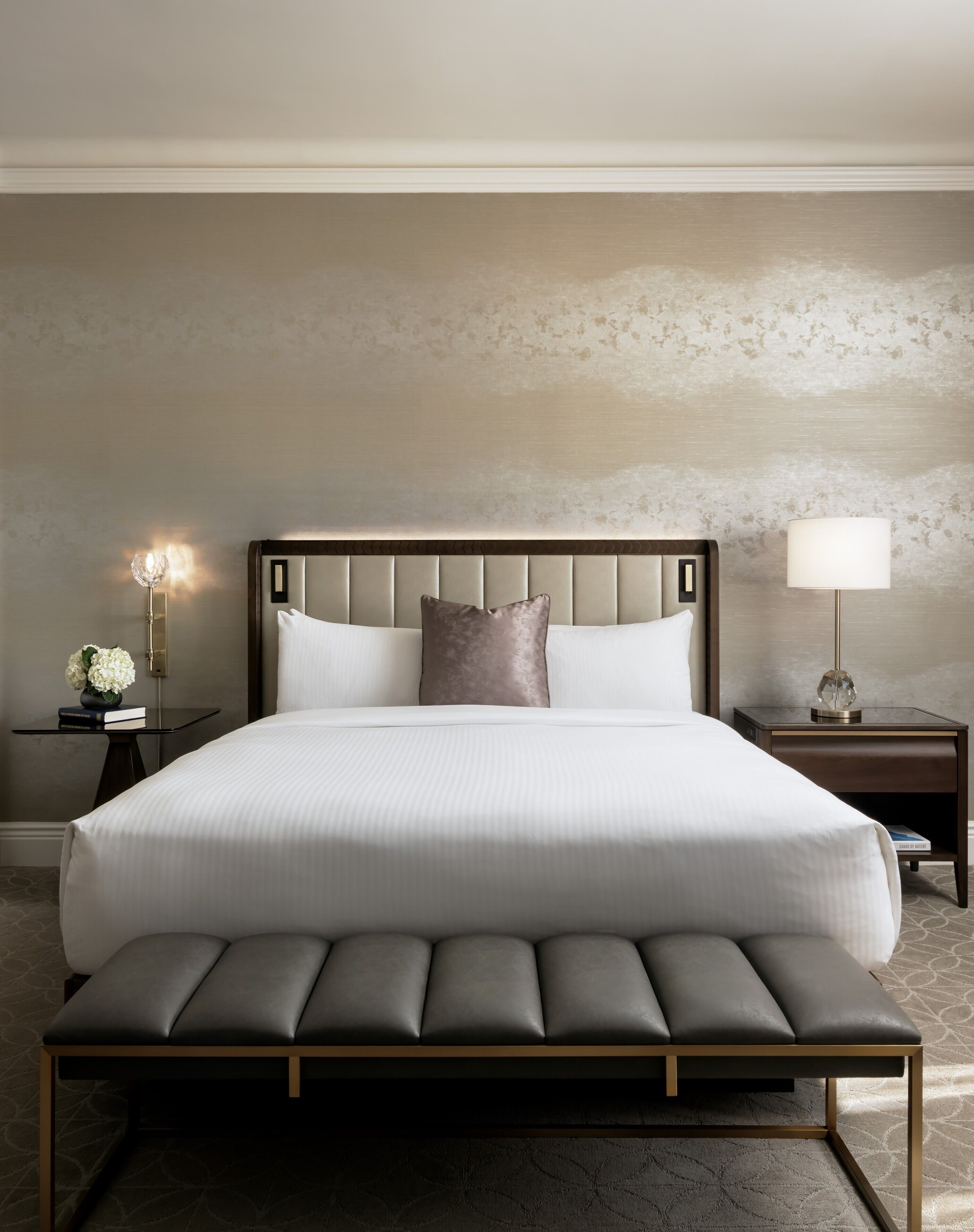 A large bed with a padded headboard and footboard, flanked by two bedside tables with lamps.