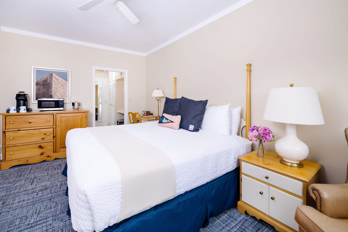 A hotel room with a bed, a wooden dresser, a nightstand, a lamp, and a picture on the wall.
