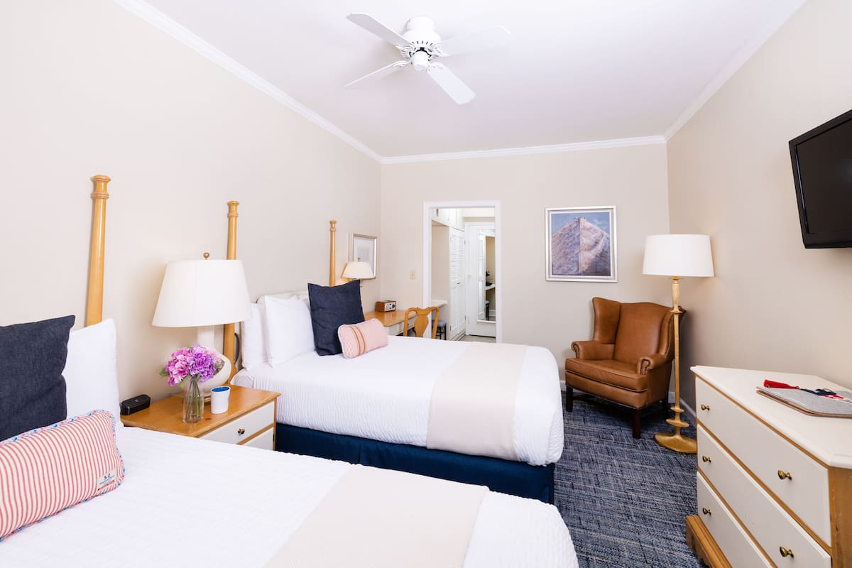 A hotel room with a bed, a chair, a dresser, a nightstand, a lamp, a ceiling fan, and a TV.