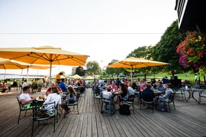 An outdoor dining area with wooden deck, tables, chairs, and yellow umbrellas. - Mission Point Resort (Mackinac Island)