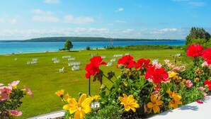 A grassy area with chairs arranged for an event, a body of water, and colorful flowers in the foreground.