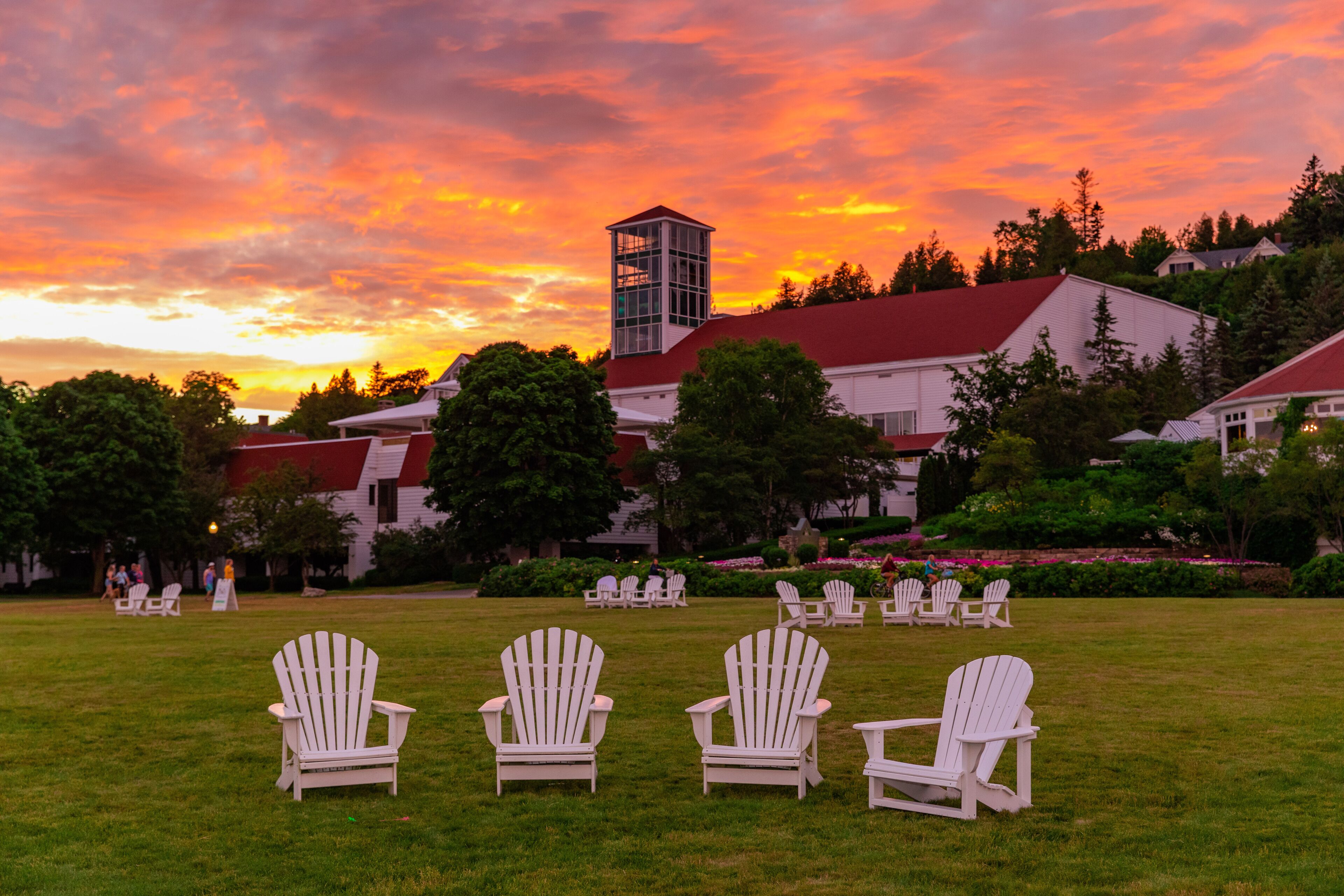 Une zone herbeuse avec des fauteuils Adirondack blancs disposés pour les invités, un bâtiment avec un toit rouge et une structure en forme de tour.
