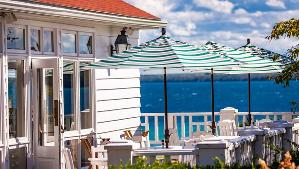 A seaside balcony with white railings, a white building with multiple windows, and a view of the ocean.