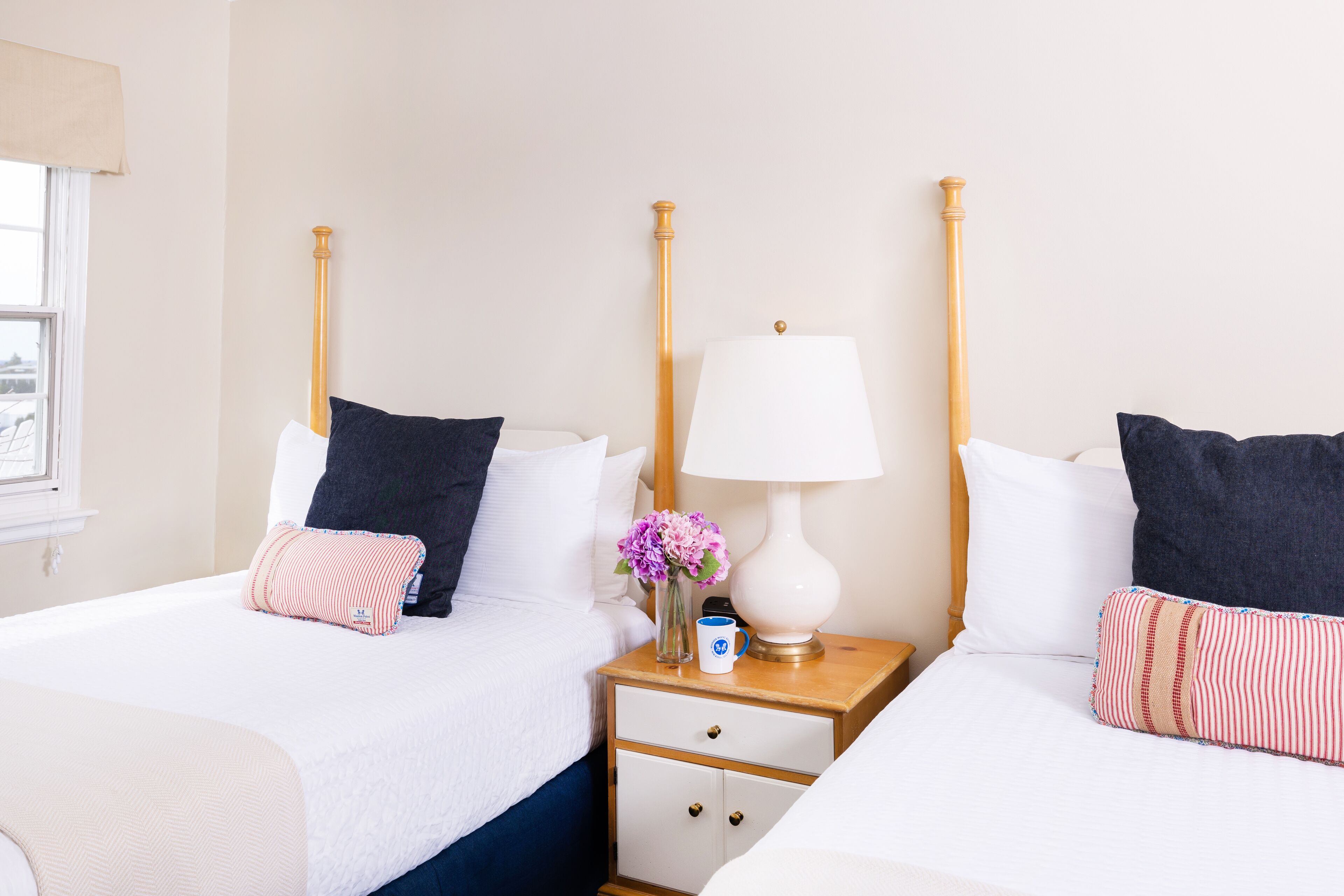 A hotel room with two beds, a nightstand with a lamp, and a vase with flowers.