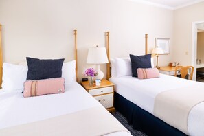 A hotel room with two beds, each with a pillow, a bedside table with a lamp, a vase with flowers, and a small table with a radio. - Mission Point Resort (Mackinac Island)