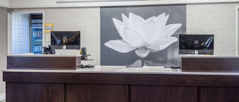 A reception desk with a large floral artwork, a refrigerator, and a flat-screen TV.