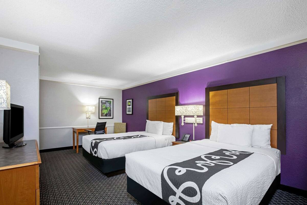 Een hotelkamer met twee bedden, een bureau, een stoel, een televisie en een lamp.