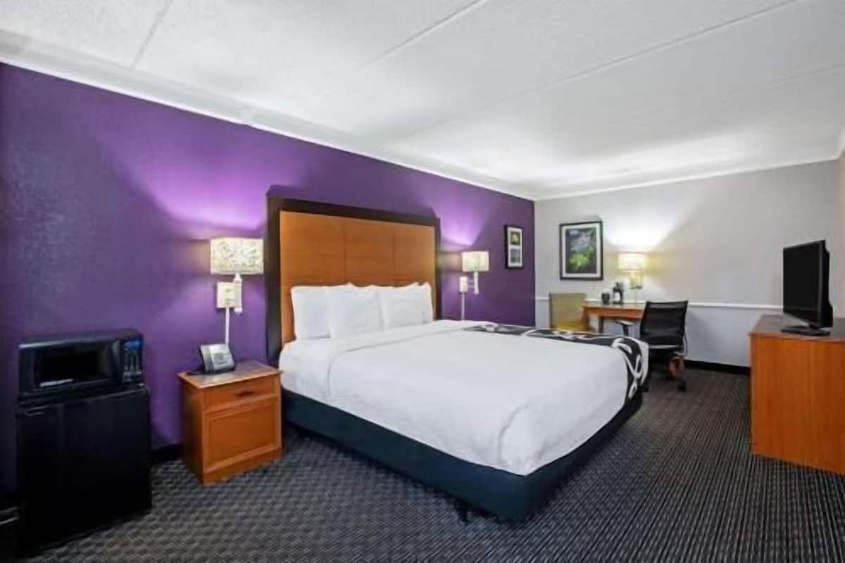 A hotel room with a bed, a desk, a chair, a TV, and a suitcase.
