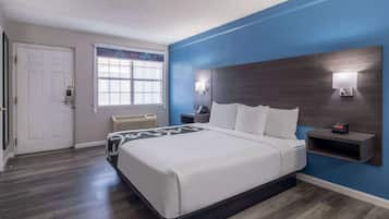 A hotel room with a bed, a nightstand, a wall clock, and a window with a view of the outside.