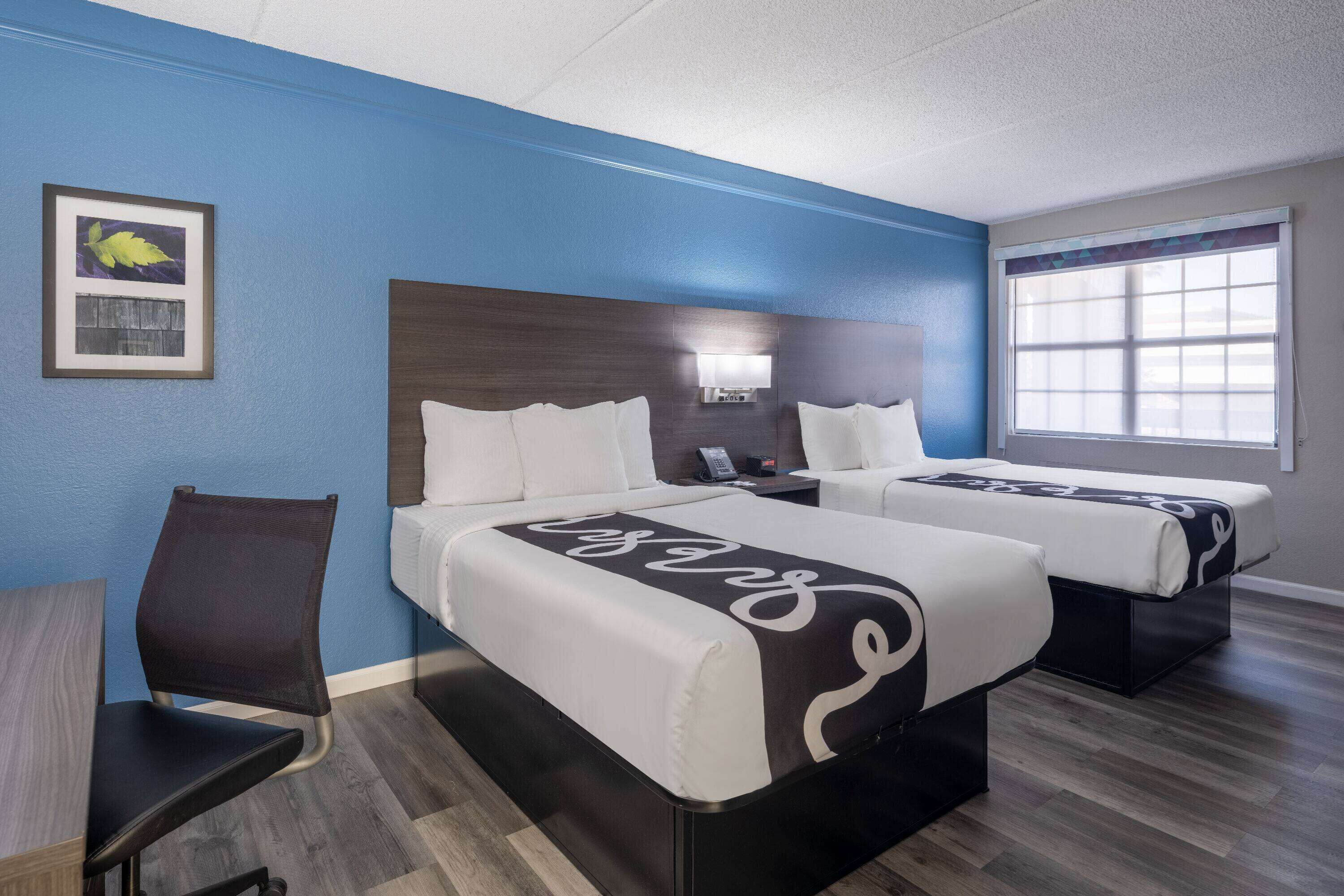 A hotel room with two beds, a desk, and a chair.