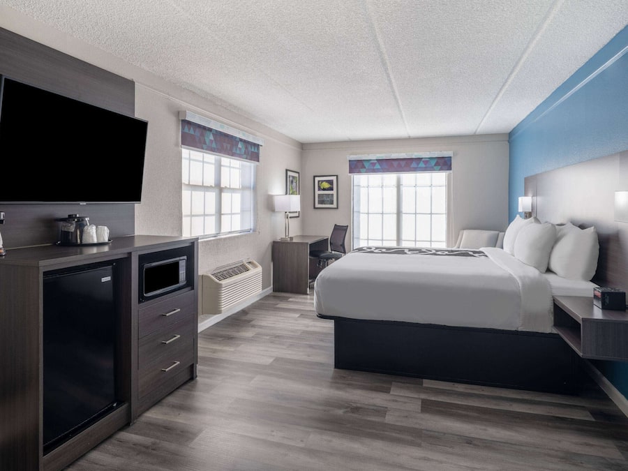 A modern hotel room with a flat-screen TV, a bed, a desk, and a chair.