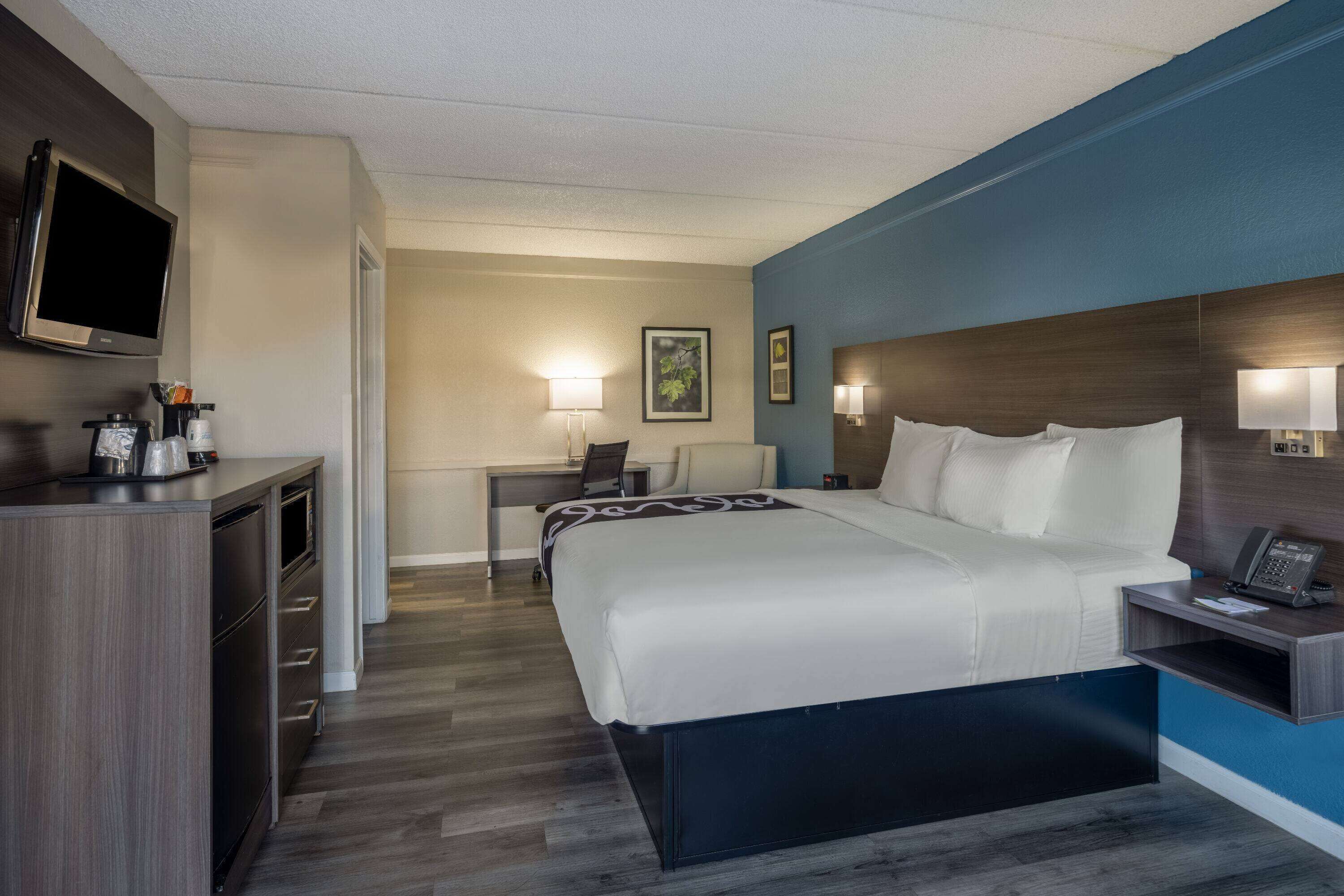 A hotel room with a bed, bedside table, desk, chair, and a TV on the wall.