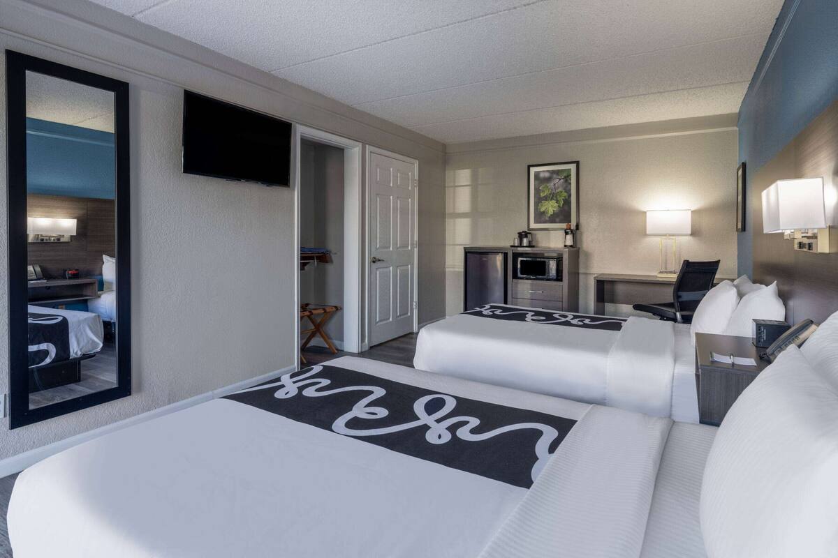 A hotel room with two beds, a TV, a desk with a chair, a microwave, and a small kitchenette.
