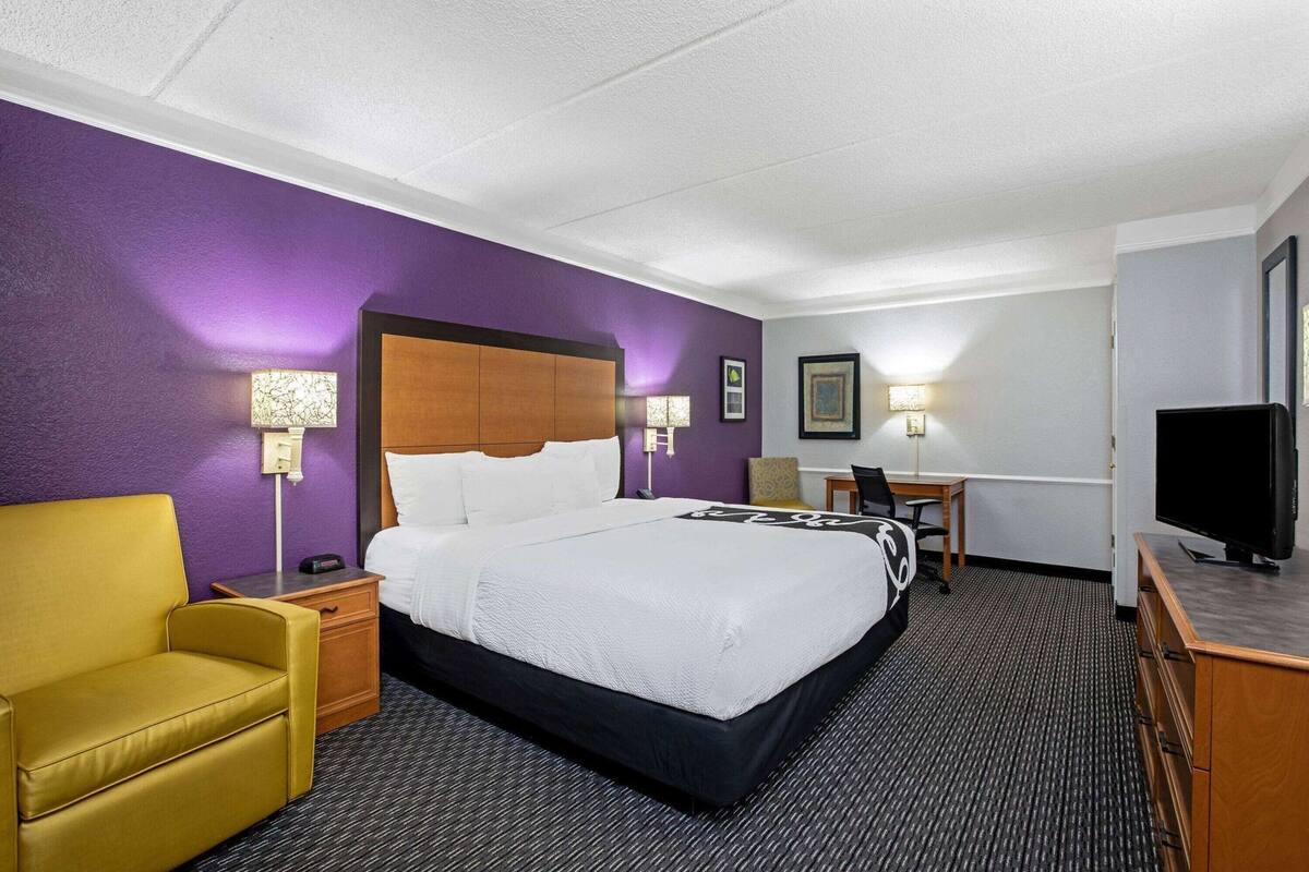 A hotel room with a bed, a desk, a chair, a television, and a lamp.