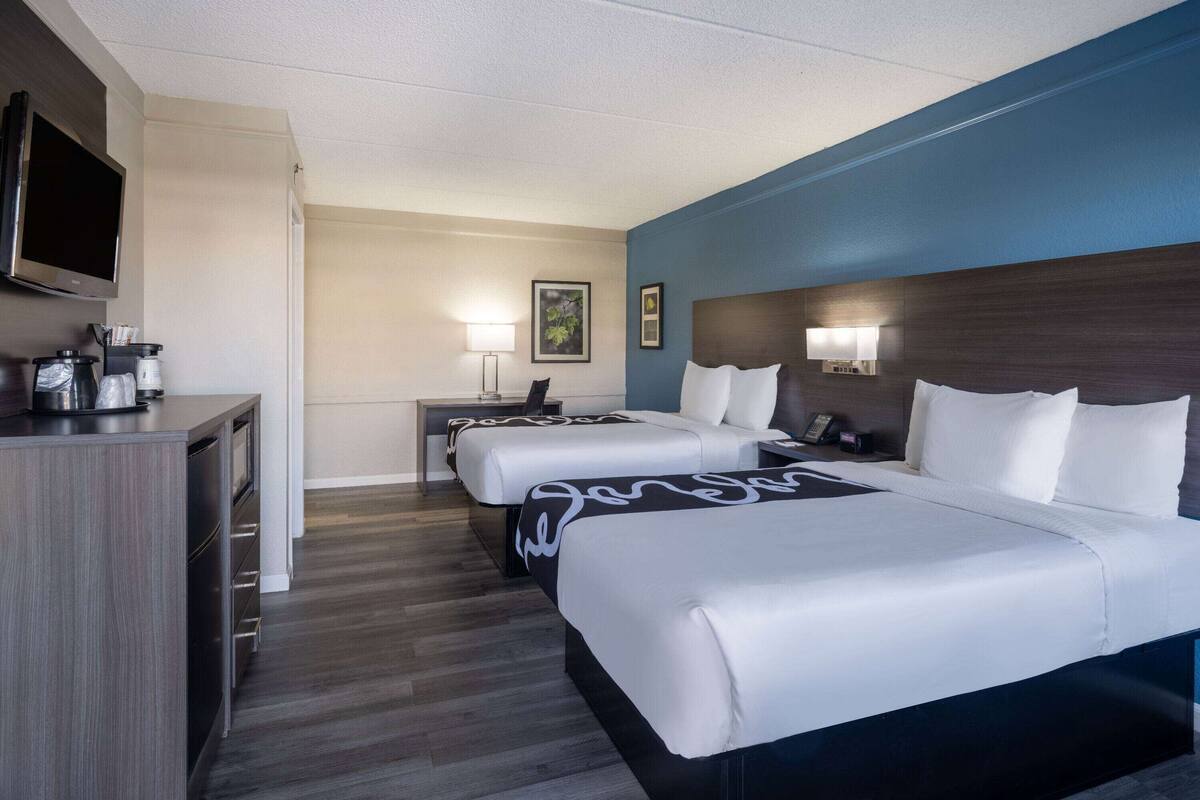 A hotel room with two beds, a desk, a TV, and a coffee maker.