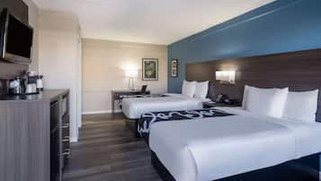 A hotel room with two beds, a desk, a TV, and a coffee maker.