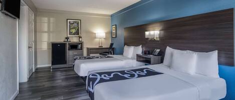A hotel room with two beds, a desk, a TV, and a minibar.
