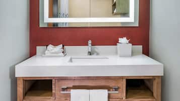 Un baño con un lavamanos blanco, un espejo y estantes de madera.