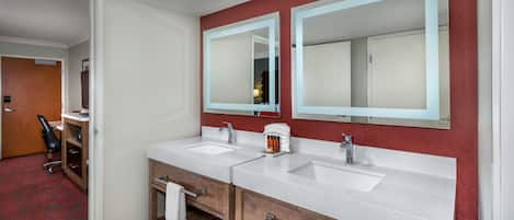A hotel bathroom with two sinks, wooden cabinets, and a red accent wall.