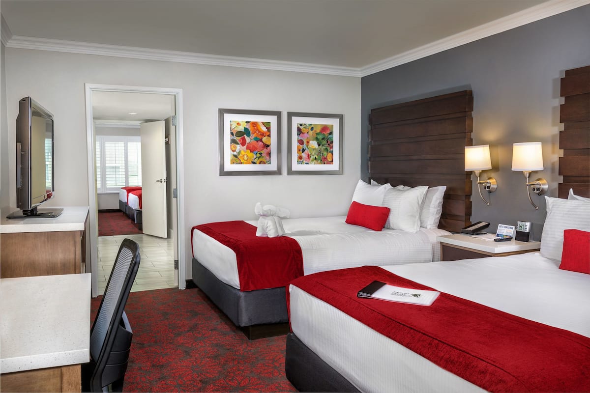 A hotel room with two beds, a desk, a chair, a mirror, and artwork on the wall.
