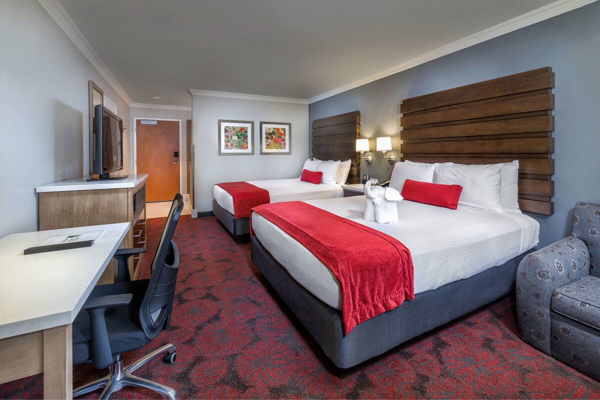 A hotel room with two beds, a desk, and a chair.